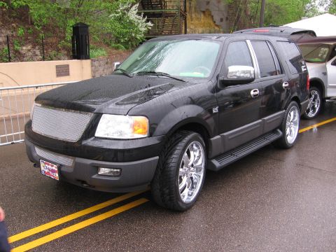 1998 GMC Sierra 1500 - This black SUV features a prominent chrome grille and custom rims, seen here on a wet day with another vehicle partially visible.