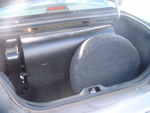 2000 Ford Crown Victoria - The trunk of a car contains a spare tire and a large subwoofer enclosure.