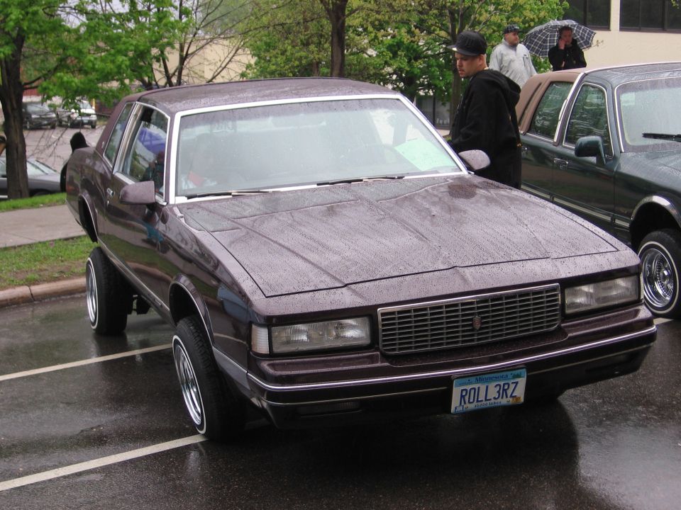 Maroon coupe with a chrome grille and whitewall tires, lowered on hydraulics