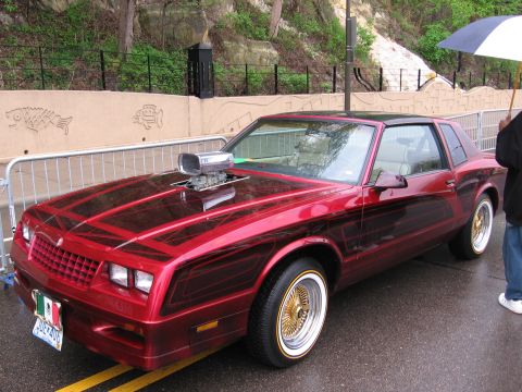 1998 GMC Sierra 1500 - A heavily customized coupe with a prominent hood scoop and gold wire wheels sits on a wet street.