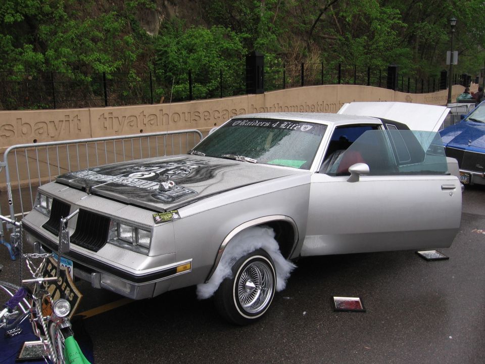 Silver coupe with custom hood art, smoke from wheel well, and open doors