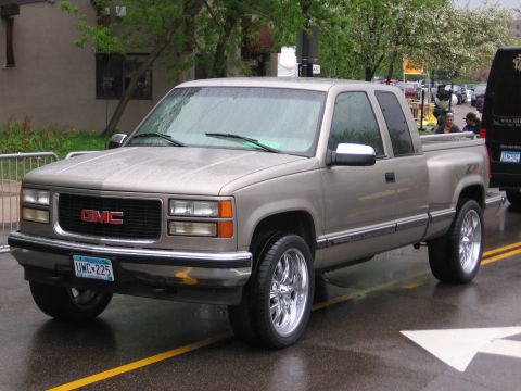 1998 GMC Sierra 1500 - A tan GMC pickup truck is parked on a wet street with yellow lines.