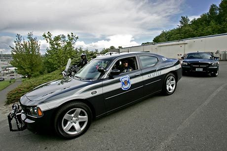 2000 Ford Crown Victoria - Two Seattle Police Department cars are parked on a road with a wooded area and buildings in the background.