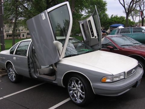 1998 GMC Sierra 1500 - This two-tone sedan features custom lambo doors and chrome rims, parked at an outdoor event.