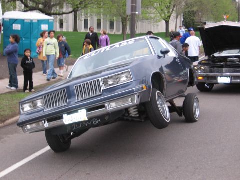 1998 GMC Sierra 1500 - A customized Oldsmobile Cutlass is displayed with its hydraulic suspension raised, while another vehicle waits in the background.