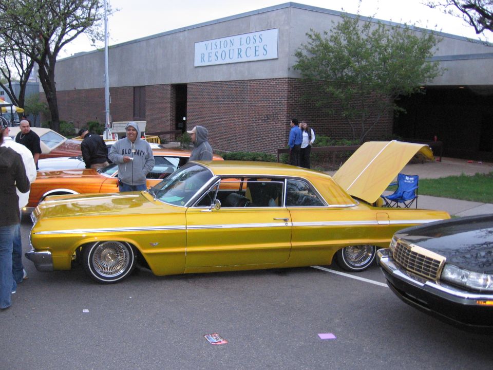 Yellow 1964 Chevrolet Impala lowrider with trunk open, side view