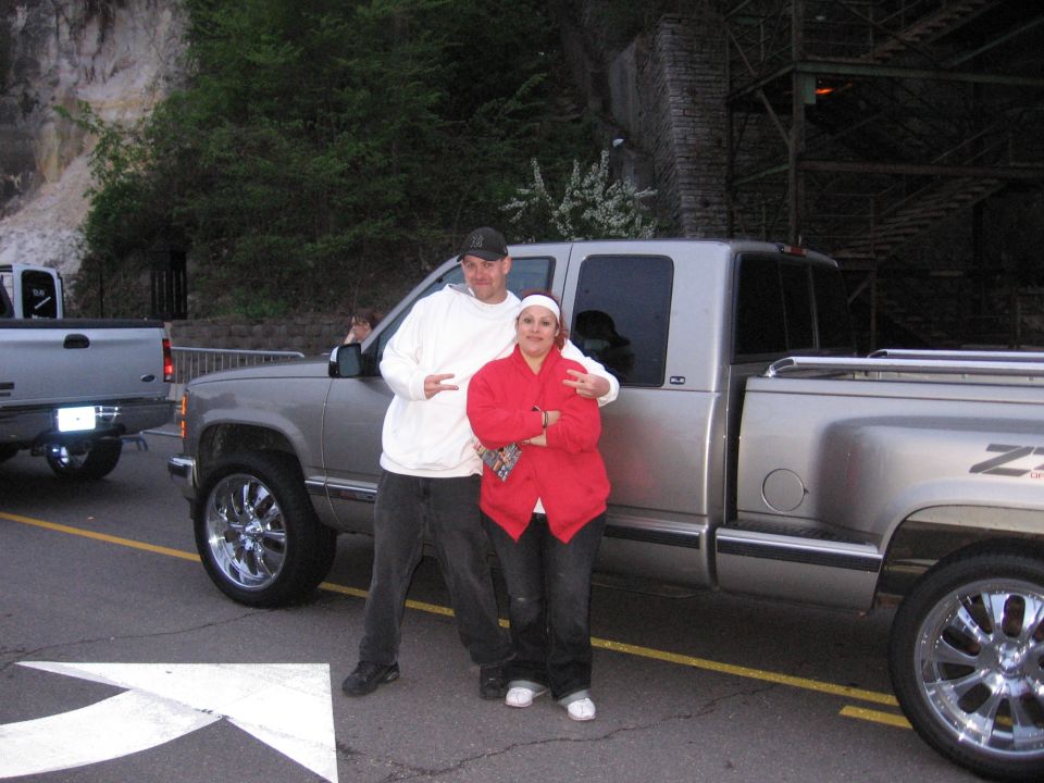 Couple posing next to a silver 1998 GMC Sierra 1500 pickup truck with custom rims