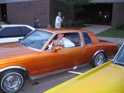 1998 GMC Sierra 1500 - A man sits in a customized orange coupe with a unique plaid interior, parked next to other vehicles.