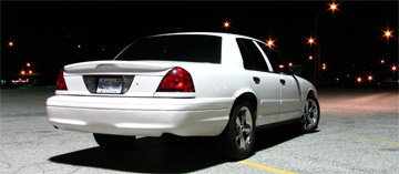 2003 Ford Crown Victoria - A white 2003 Ford Crown Victoria is parked in a lot at night, viewed from the rear quarter panel.