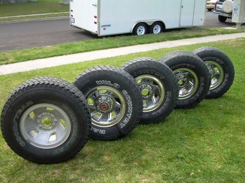 1986 Ford Bronco - Set of four Goodyear Wrangler RT/S tires with chrome rims displayed on a lawn.