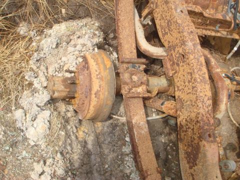1996 Ford Bronco - Close-up of a heavily rusted rear axle and leaf spring assembly lying on the ground.