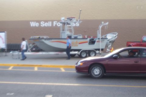1998 Ford Crown Victoria - A boat on a trailer is parked in front of a building. A maroon car is in the foreground.