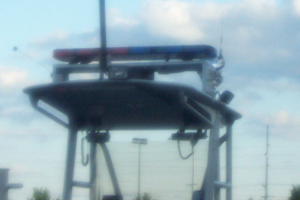 Dark vehicle roof with red and blue light bar, antenna, and spotlight against a cloudy sky