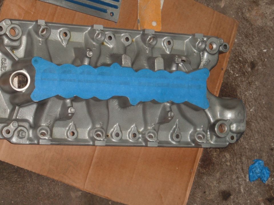 Close-up of an engine intake manifold with blue tape applied to the gasket surface