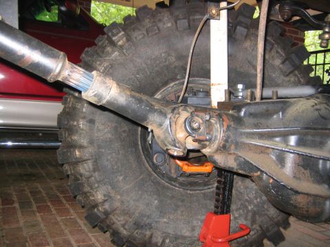 1979 Ford Bronco - Close-up view of a vehicle's rear axle and driveshaft, with a large tire and a red vehicle in the background.