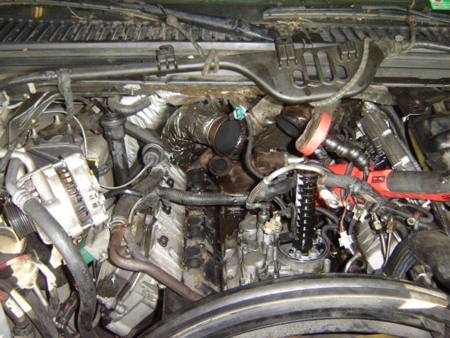 Engine bay with hoses, wires, and turbocharger components visible. Some parts appear dirty and oily
