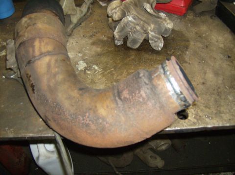 1996 Ford Probe - A rusty exhaust pipe section with visible weld repairs sits on a workbench.