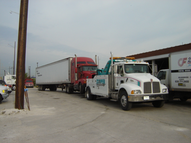 White tow truck with 'Cooper' logo towing a red semi-trailer truck