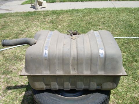 1986 Ford Bronco - A fuel tank, likely for a truck or SUV, is shown outdoors resting on a tire.