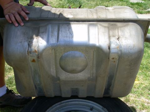 1986 Ford Bronco - A person holds a metal fuel tank, which is placed on top of a spare tire outdoors.