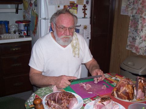 1992 Ford Bronco - A man with a beard carves a ham in a kitchen setting, with other hams visible on the table.