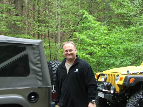 1996 Ford Bronco - A man poses for a photo between two off-road vehicles in a forest setting.