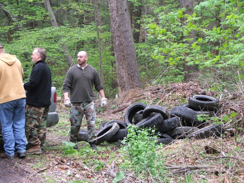 Side view of silver SUV next to pile of tires in woods