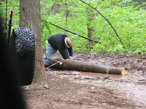 1996 Ford Bronco - A person is cutting a fallen tree on a muddy trail in a wooded area.