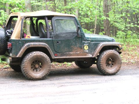 1996 Ford Bronco - A muddy Jeep Wrangler sits on a dirt road surrounded by trees, suggesting it has been off-roading.