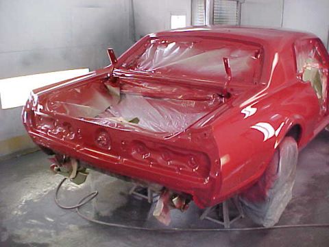 1967 Mercury Cougar - A red car is being painted in a booth, with the trunk open and parts covered.