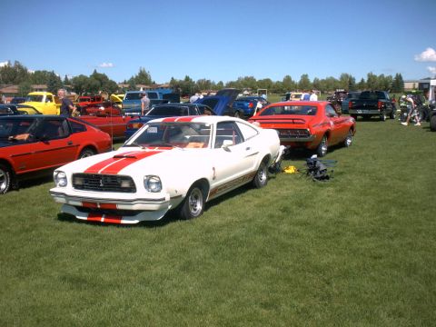 1978 Ford Mustang II - White 1978 Ford Mustang II with red racing stripes is displayed at an outdoor car show.