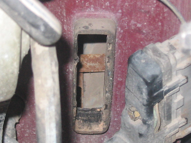 Close-up of a rusted metal bracket inside a vehicle's engine bay, next to a black electrical component