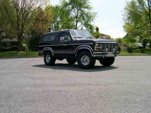 1984 Ford Bronco - This 1984 Ford Bronco is captured in a three-quarter front view, parked on asphalt under a partly cloudy sky.