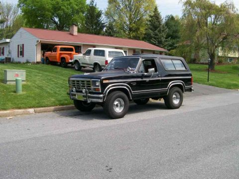 1984 Ford Bronco - A black Ford Bronco is parked in front of a house with other vehicles in the driveway.