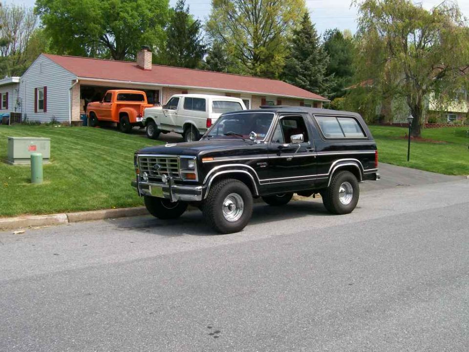 Black Ford Bronco parked on street, orange Ford pickup and white Bronco in driveway