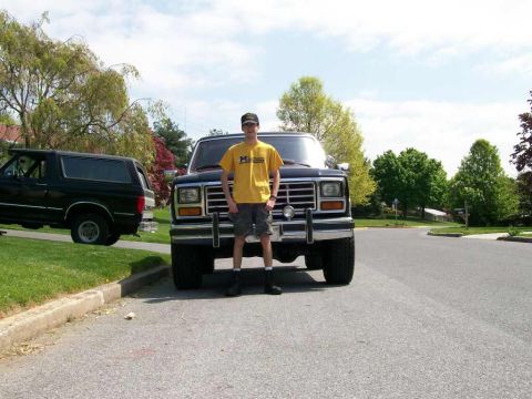 1984 Ford Bronco - Two Ford Broncos are visible in a residential area, with a person standing in front of the larger one.