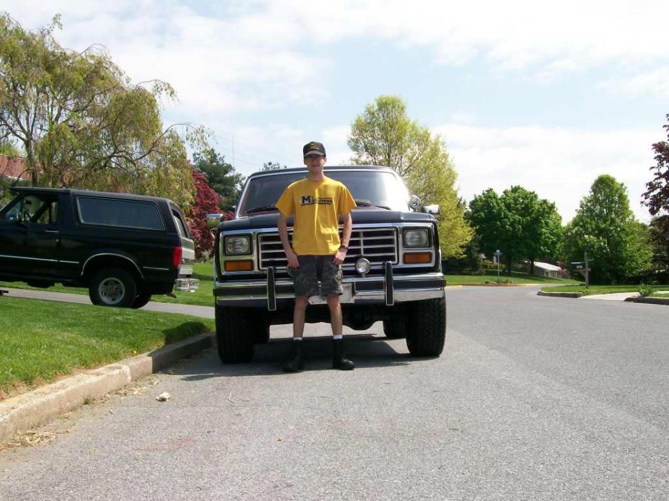 Person in yellow shirt stands before a dark Ford Bronco; another black Bronco is parked to the left