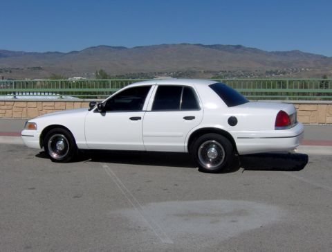 1999 Ford Crown Victoria - Side view of a white sedan parked outdoors with a mountainous landscape behind it.