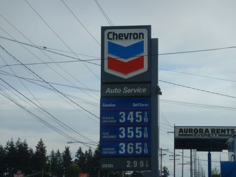 2000 Ford Crown Victoria - A gas station sign displays fuel prices under a cloudy sky, with power lines overhead.