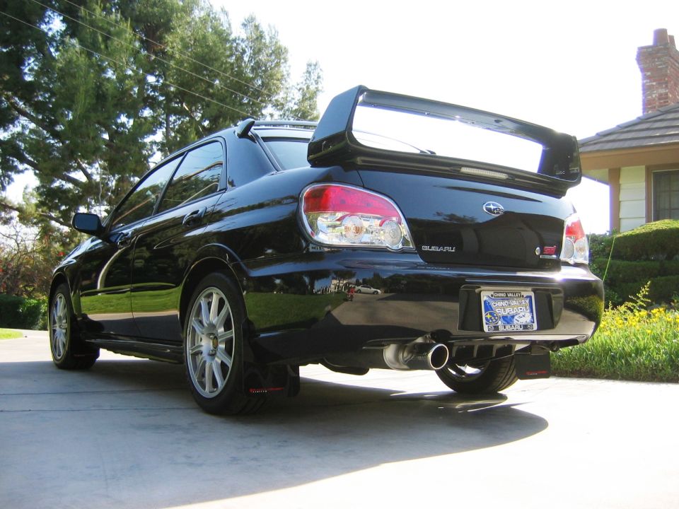 Black Subaru Impreza STI sedan rear three-quarter view with tall wing spoiler in a driveway.