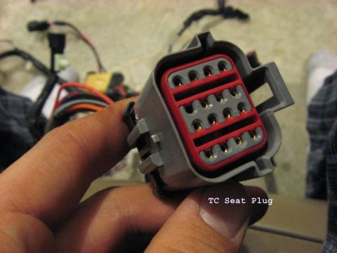 2001 Ford Crown Victoria - A close-up shows a multi-pin electrical connector, labeled 'TC Seat Plug', held by a hand.