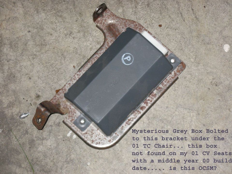 Gray Ford electronic module bolted to a rusty seat bracket on a concrete floor
