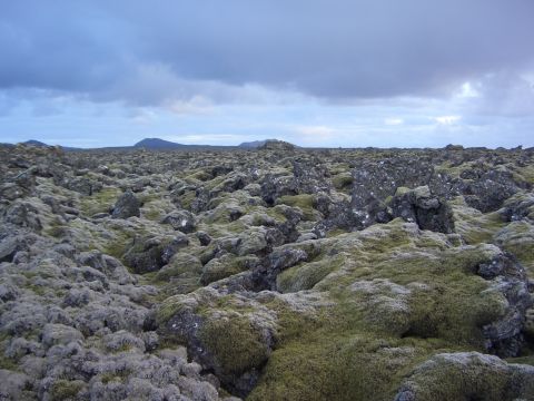 1974 Ford Bronco - A vast, rocky landscape covered in moss stretches towards distant hills under a dramatic, cloudy sky.