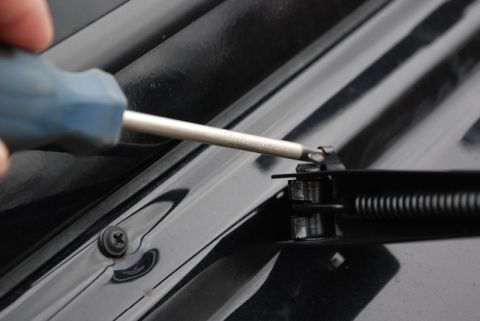 1996 Ford Bronco - Screwdriver adjusting a hood hinge mechanism on a black vehicle.