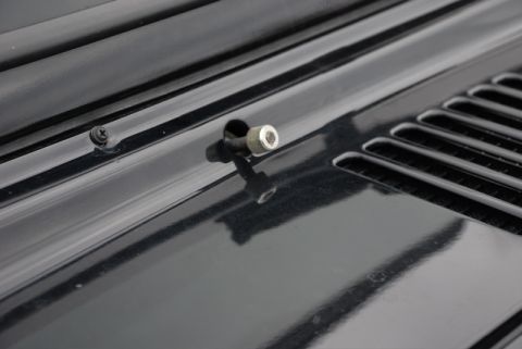 1996 Ford Bronco - Hood latch mechanism shown on a black vehicle hood, with vent detail visible.