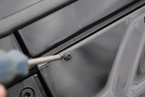 1996 Ford Bronco - A screwdriver is used to adjust a screw on a black car component, likely part of the hood mechanism.