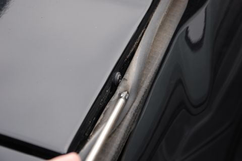 1996 Ford Bronco - Close-up of a car's hood edge and rubber seal being adjusted with a screwdriver.