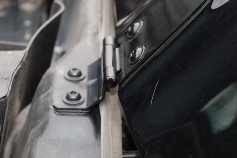 1996 Ford Bronco - Detail of a vehicle's hood hinge mechanism, showing the mounting screws and hinge pin.