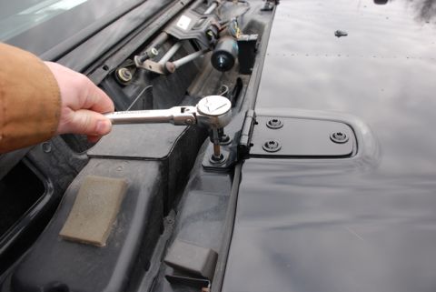 1996 Ford Bronco - A hand is shown adjusting the hood hinge of a vehicle with a socket wrench.