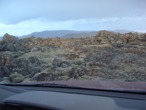 1974 Ford Bronco - A desolate landscape of rocks and moss stretches towards distant hills under an overcast sky.